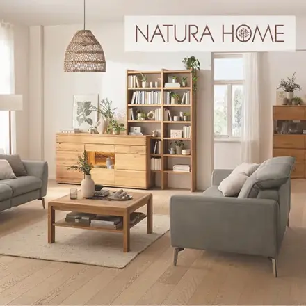 Wohnzimmer mit grauen Sesseln, Holzmöbeln, Regal und Logo NATURA HOME